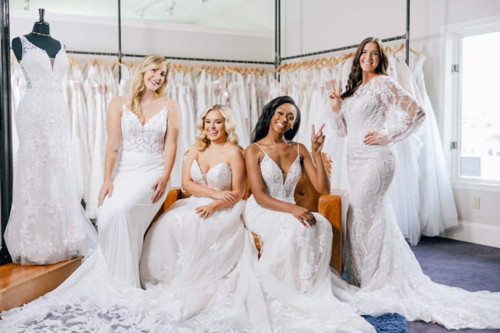4 smiling women in various bridal dresses looking at camera