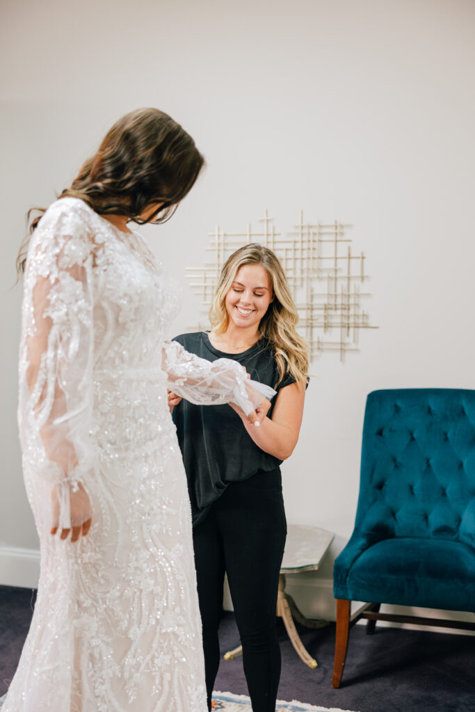 smiling bridal stylist helping bride try on dress