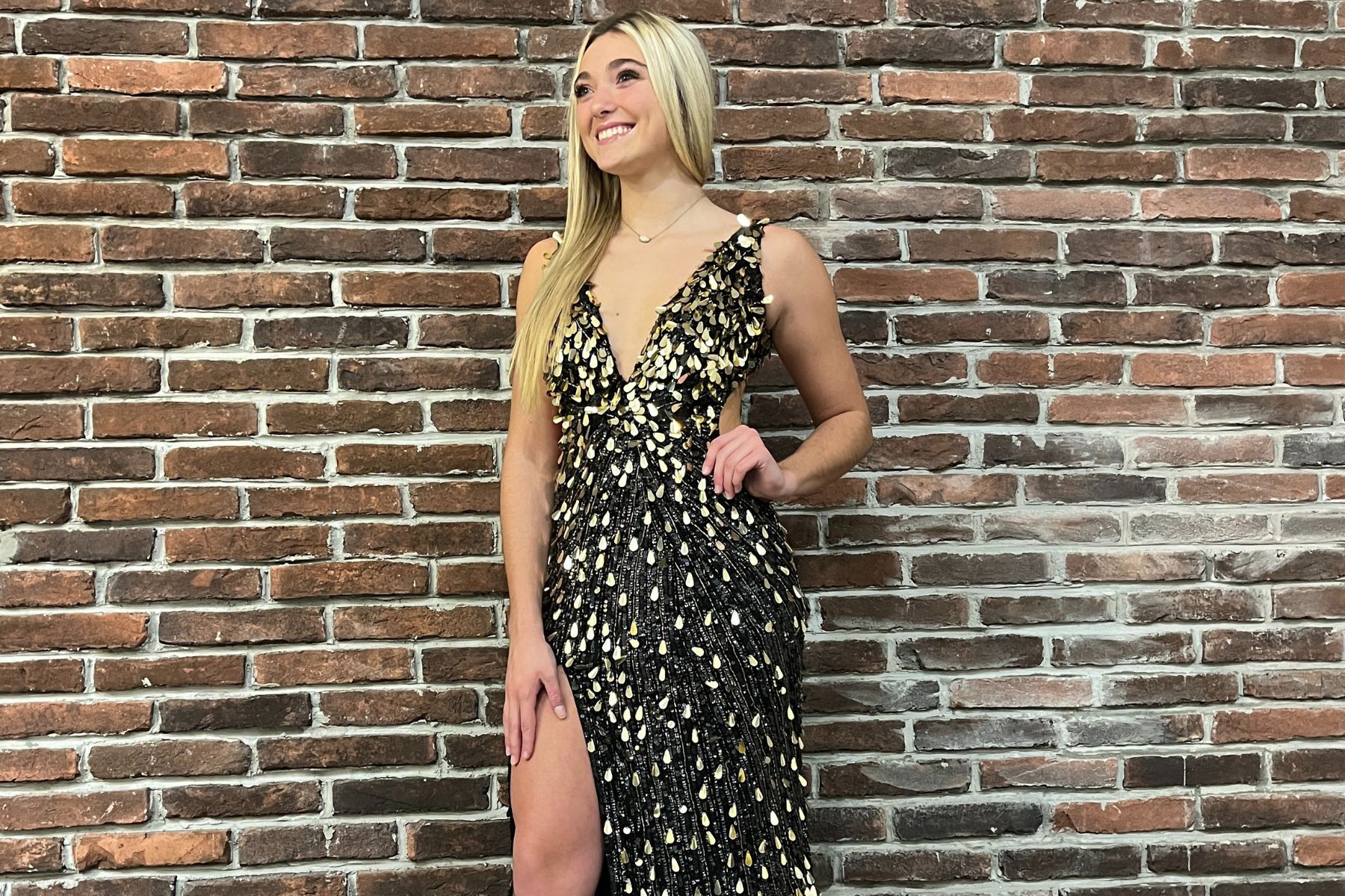 young woman in a black and gold formal gown in front of a brick wall