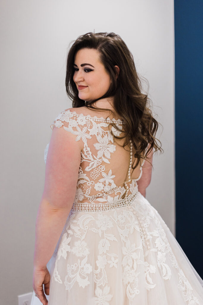 plus size bride looking over her shoulder in a lace wedding gown with a sheer back