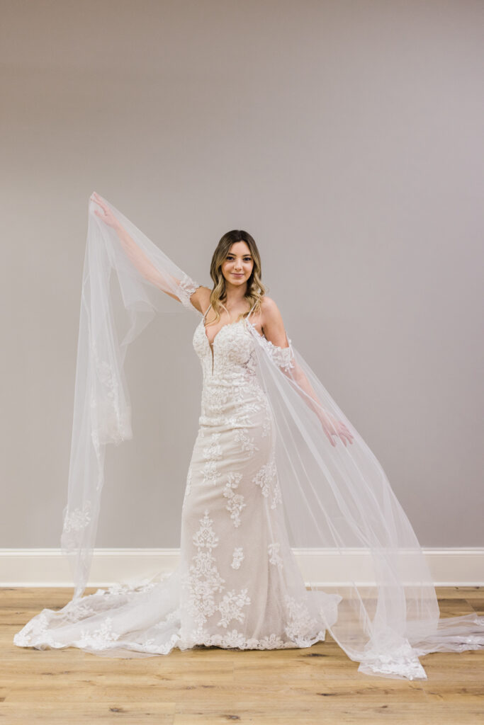 Bride dancing in wedding gown with fun sleeves standing in front of grey wall
