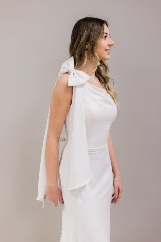 bride posing in simple, fitted wedding gown with a bow sleeve on her shoulder 