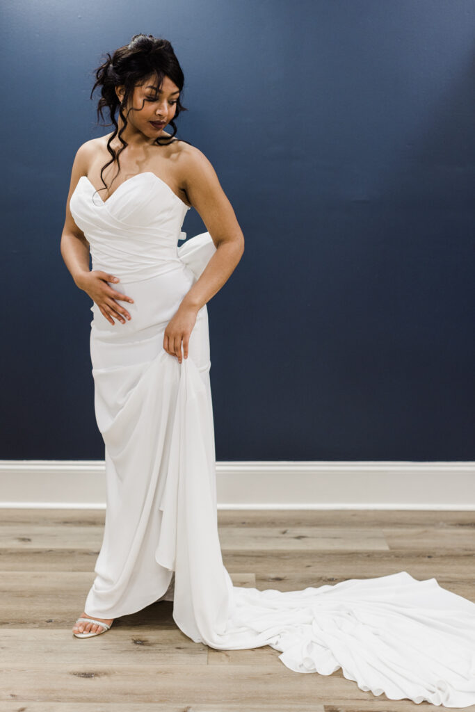 bride posing in simple wedding gown with a large bow detail on the back in front of navy blue wall