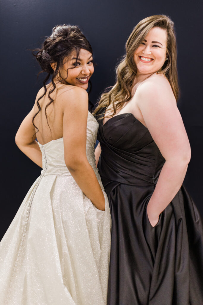 2 brides posing in front a navy colored wall. one wearing a champagne colored gown and the other wearing a black wedding dresss