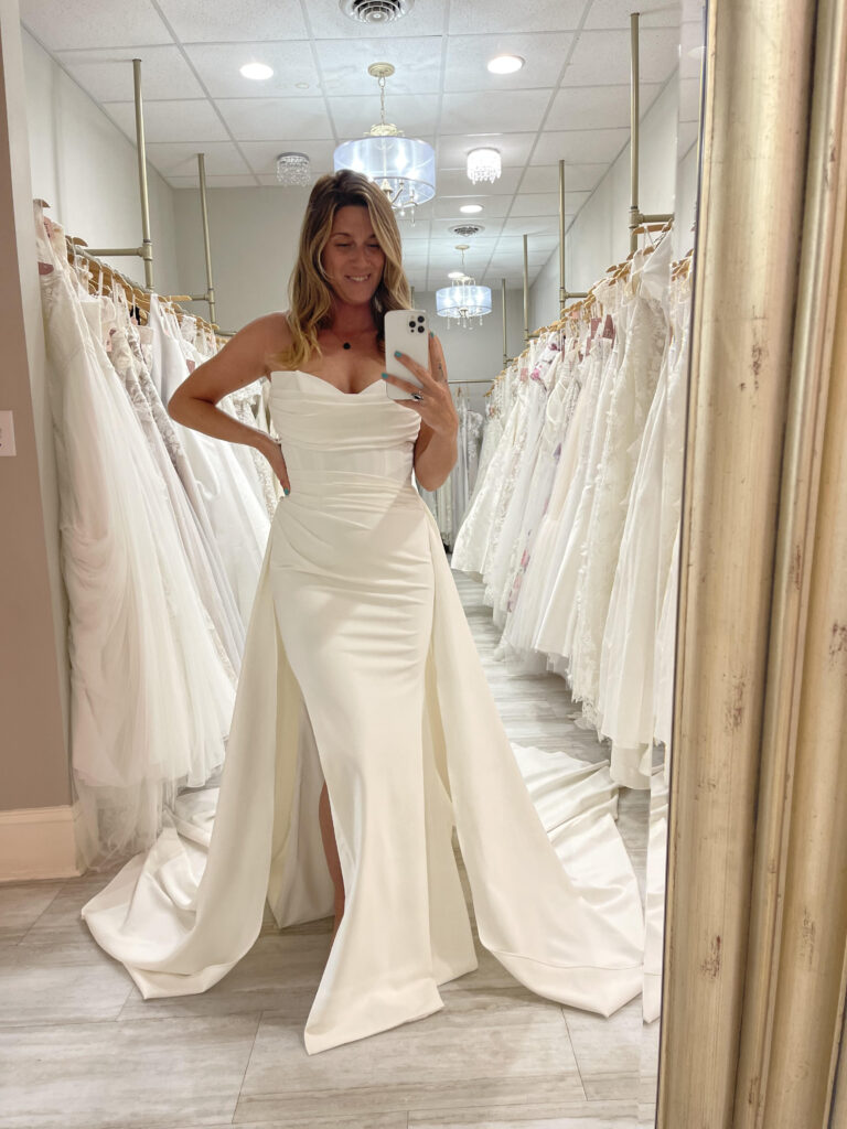 A bride taking a selfie in the mirror at Amanda's Touch in a wedding dress with an overskirt