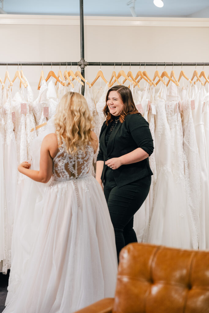 stylist laughing with bride while looking at wedding dresses