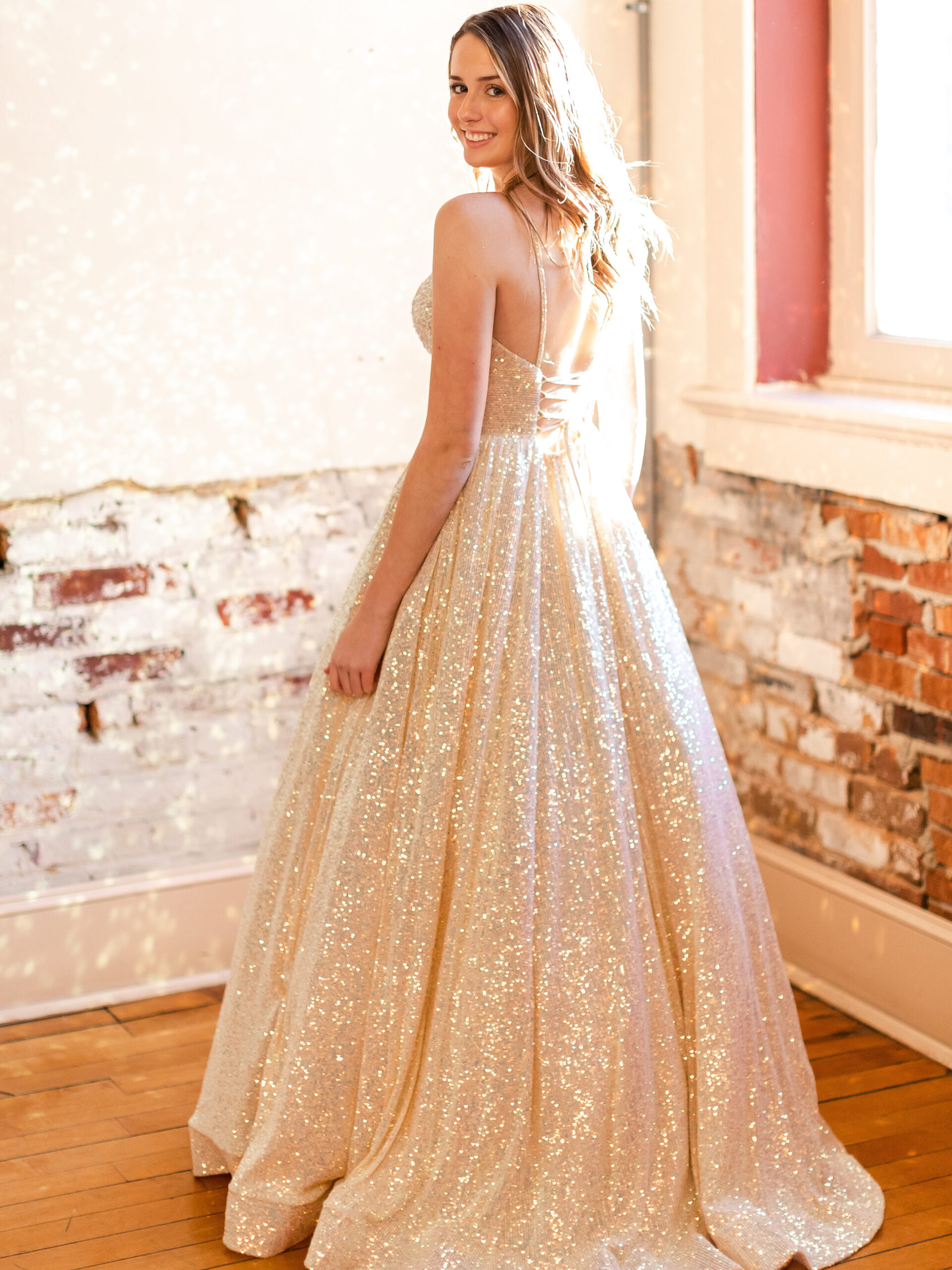 girl posing in sparkly champagne colored prom dress in front of white brick wall