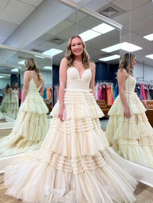 girl posing in champagne colored prom dress with ruffles in front of mirror