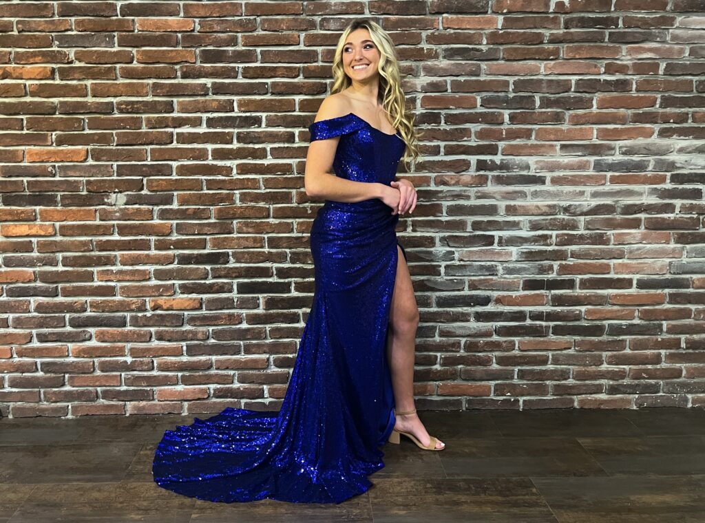 girl posing in front of brick wall wearing blue sparkly prom dress