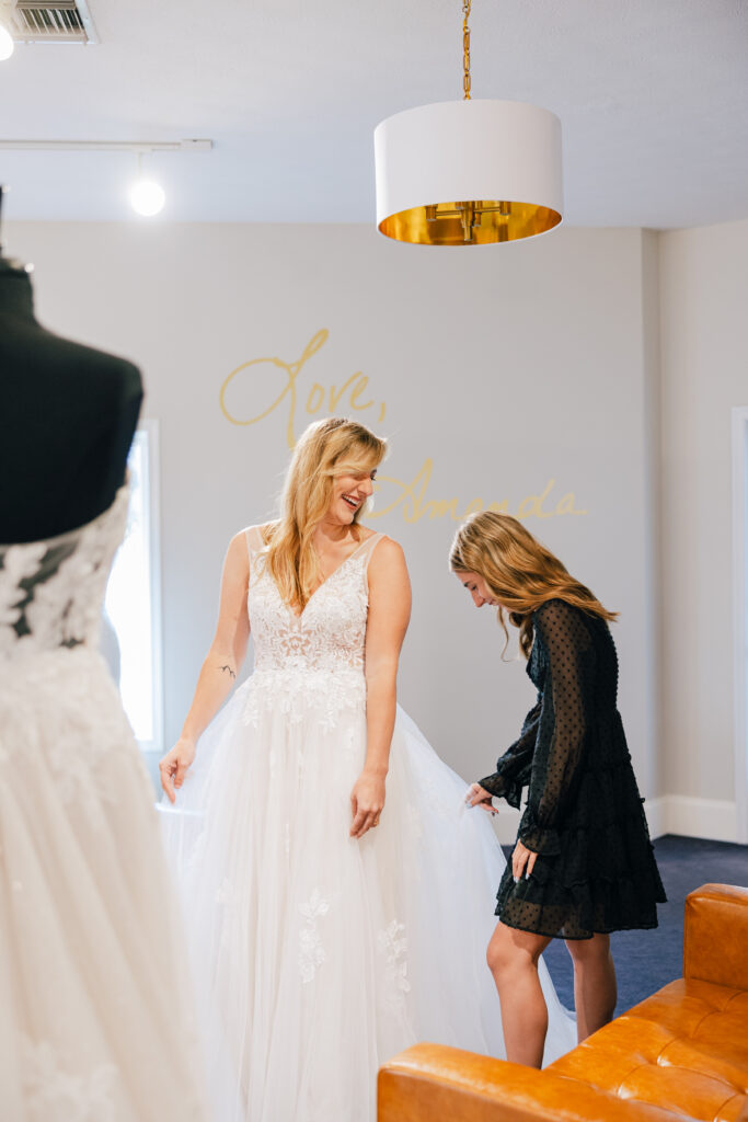 A bride and one of her bridesmaids smile together as she finds her perfect wedding gown