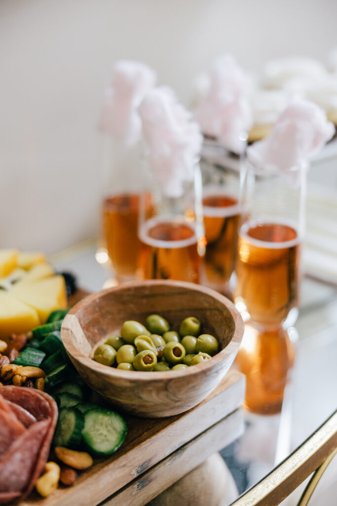 a bowl of olives on a charcuterie board filled with meats and cheeses, with champagne in the background