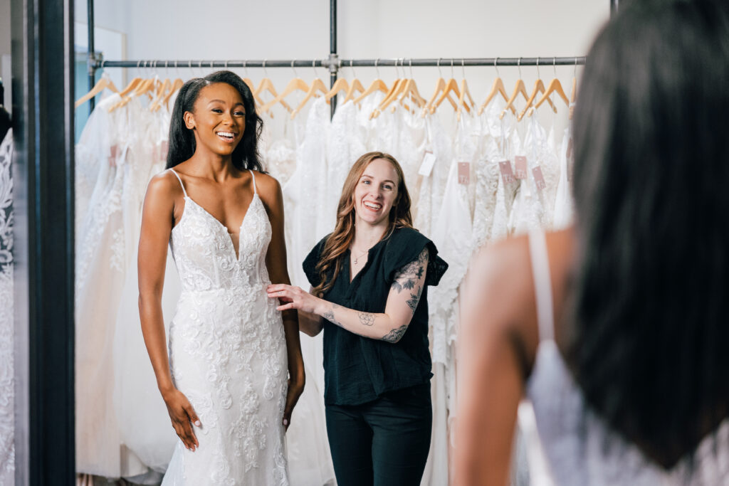 a bride and an expert bridal stylist smiling together as a bride tries on her dream wedding dress