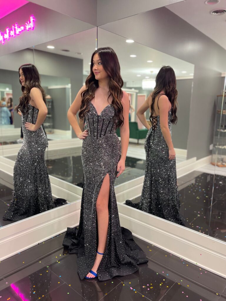 A young woman posing in a dark, sparkly prom dress in front of mirrors at Amanda's Touch