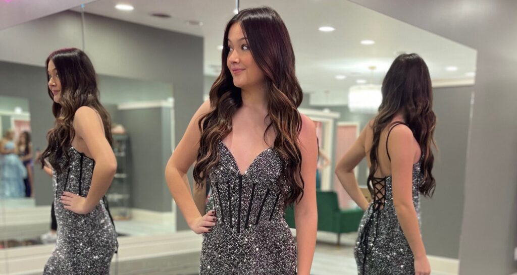 A young woman posing in a dark, sparkly prom dress in front of mirrors at Amanda's Touch