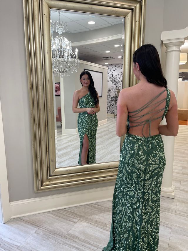 A student smiling as she looks at her green prom dress in front of a mirror at Amanda's Touch