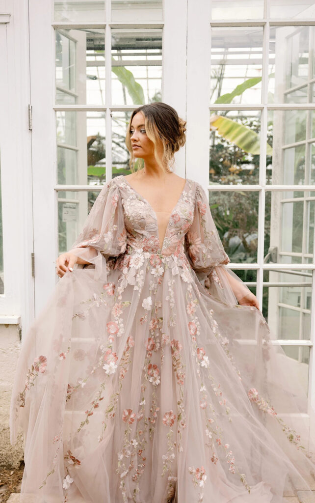 A bride wearing a blush wedding dress with a plunging neckline and floral details