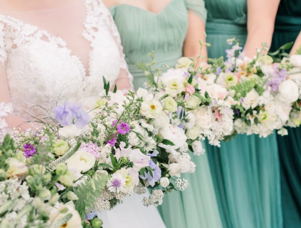 A group of bridesmaids in green dresses and holding bouquets of beautiful white and purple flowers.