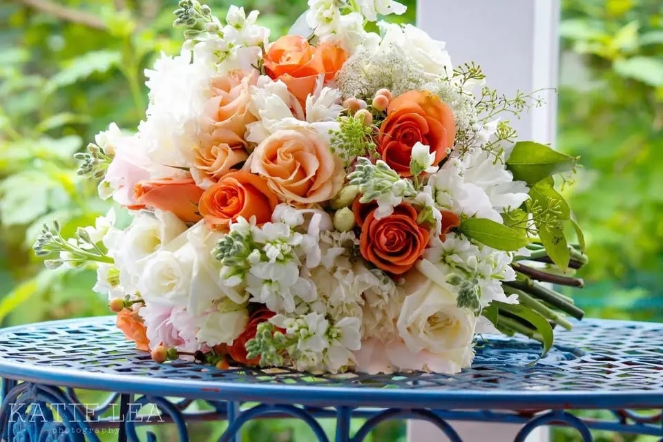 A colorful bridal bouquet with orange, pink, and white roses, along with other beautiful flowers.