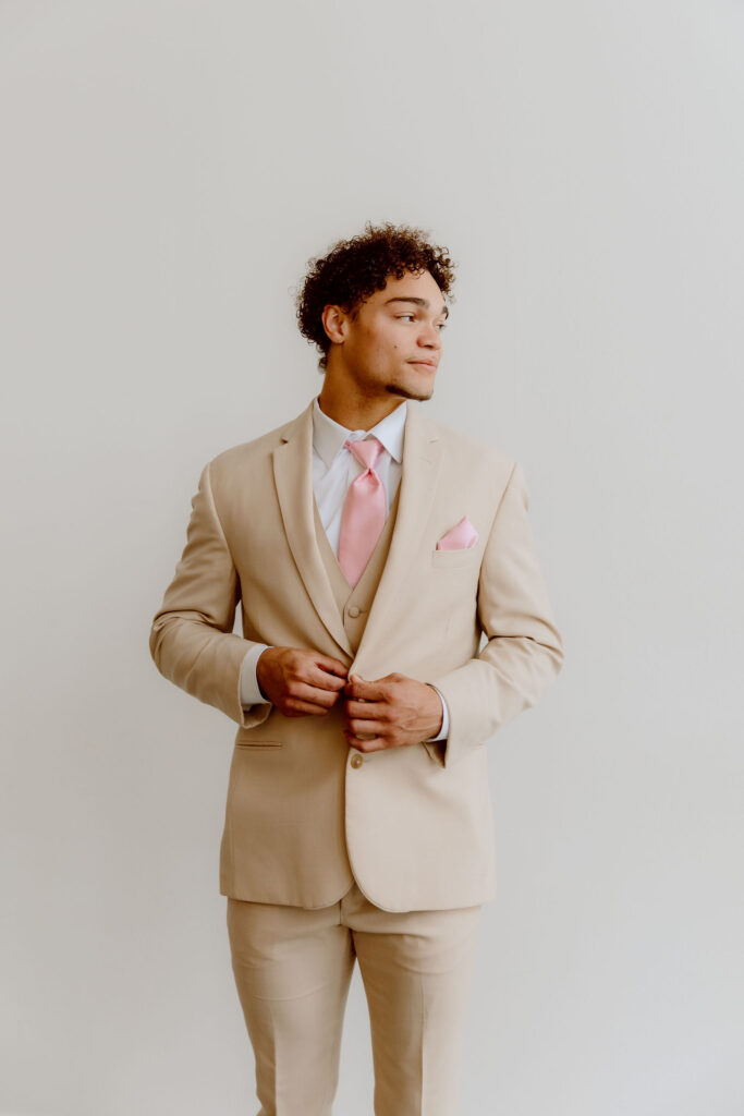 A man buttoning his tuxedo jacket, wearing a tan havana suit