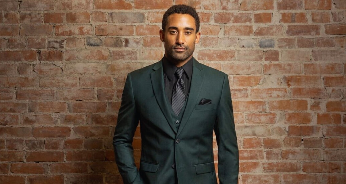 A man in a dark green tuxedo a color known as "hunter green" standing in front of a brick wall