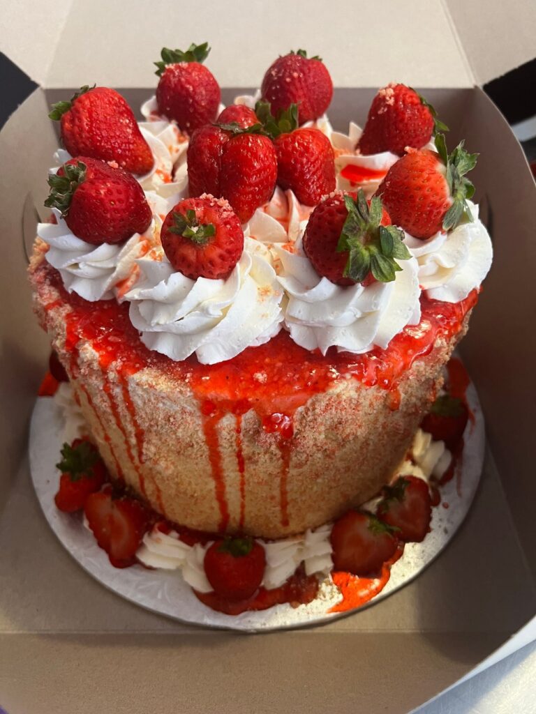 A stunning vanilla wedding cake topped with strawberry sauce, whipped cream, and strawberries.