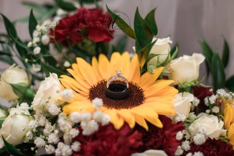 A sunflower wedding ring holder on a bouquet of red and white flowers with green leaves.