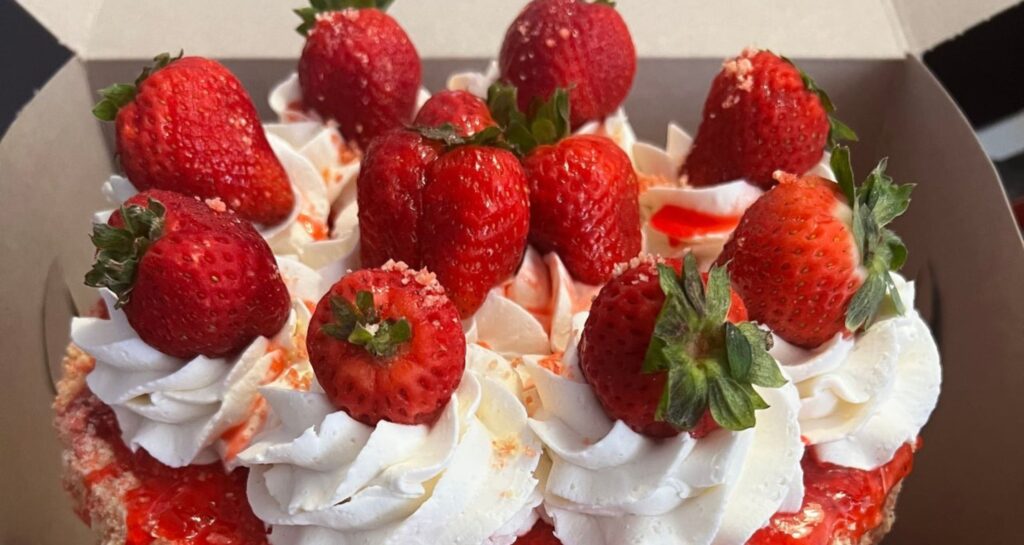 A stunning vanilla wedding cake topped with strawberry sauce, whipped cream, and strawberries.