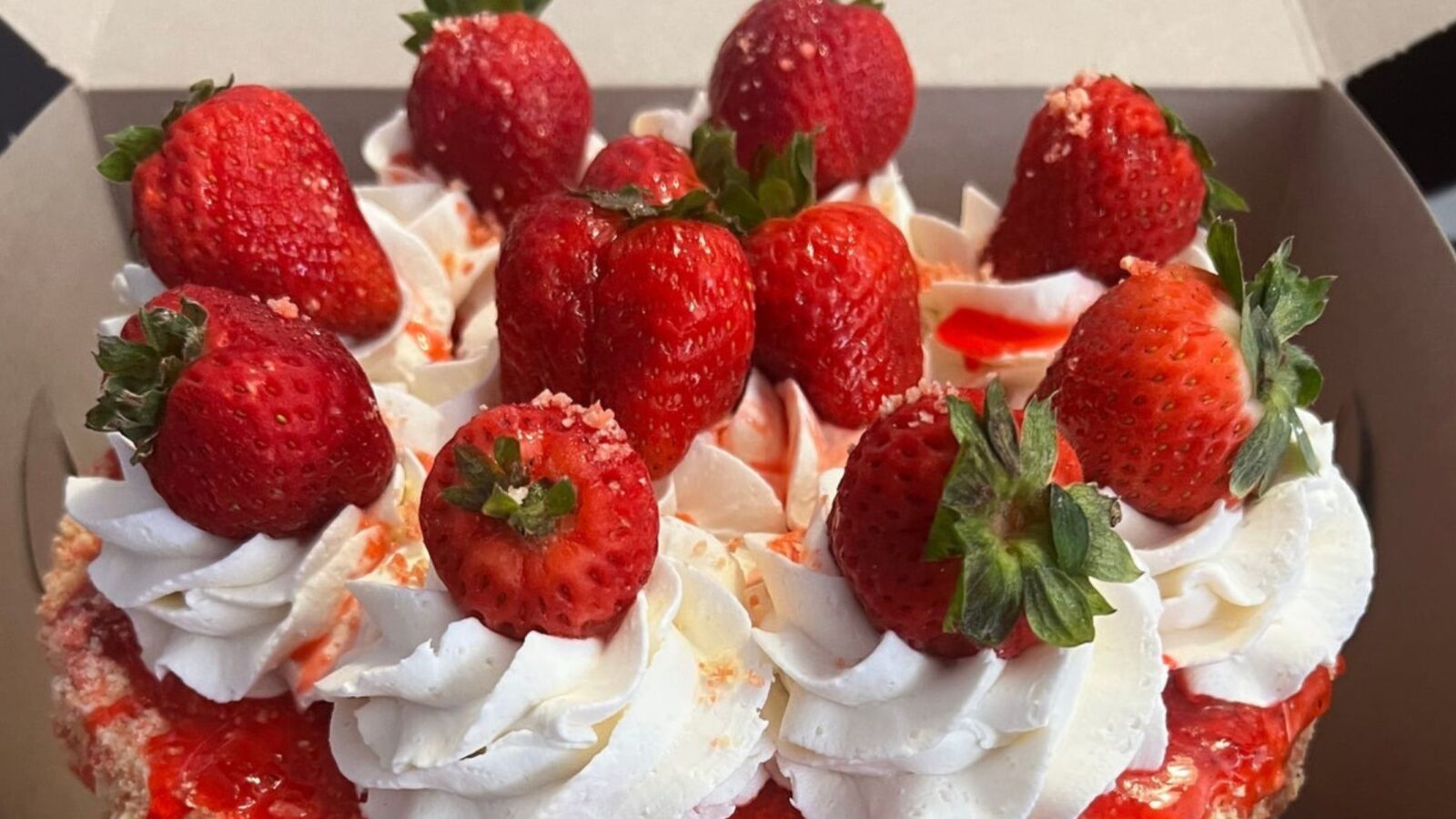 A stunning vanilla wedding cake topped with strawberry sauce, whipped cream, and strawberries.