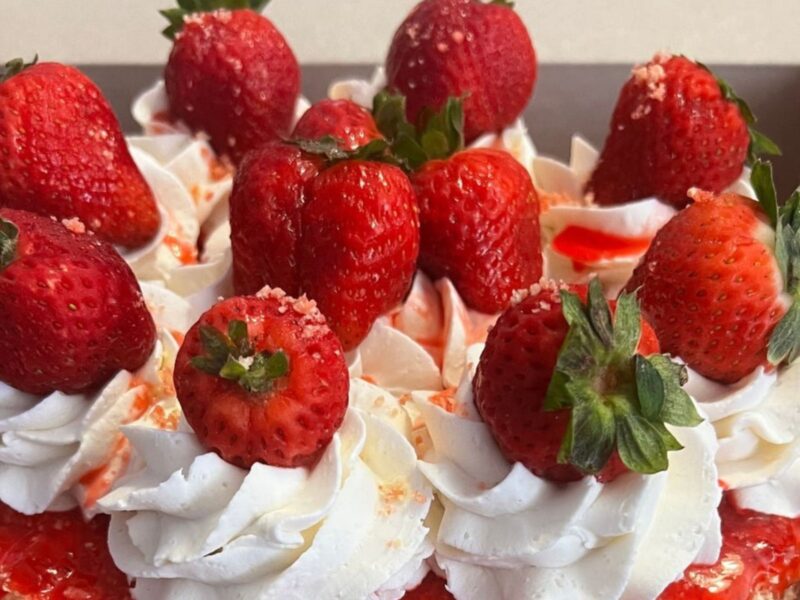 A stunning vanilla wedding cake topped with strawberry sauce, whipped cream, and strawberries.