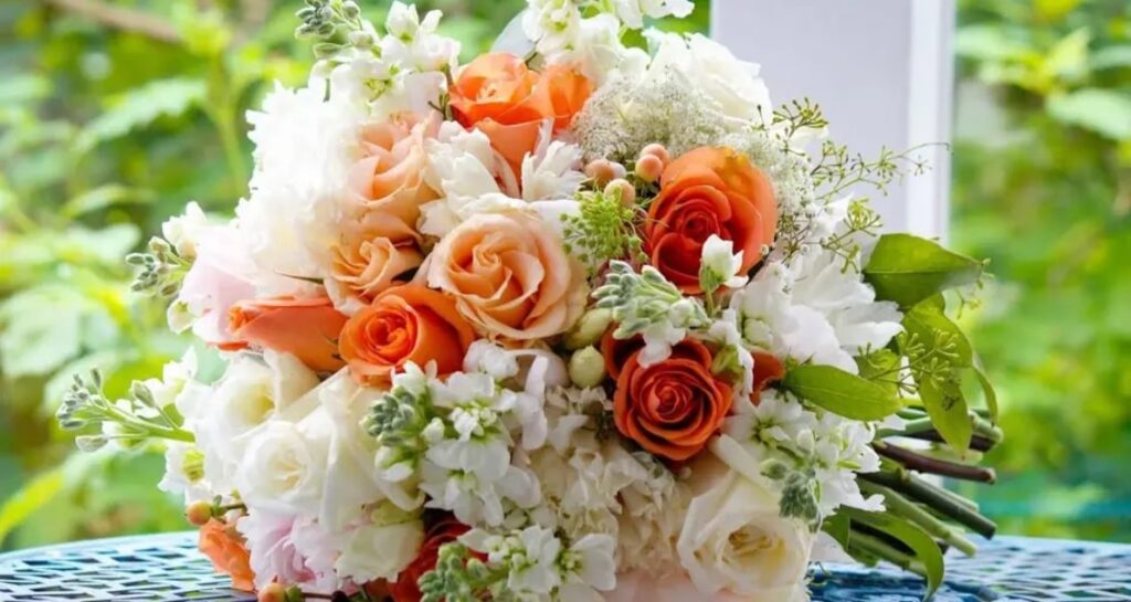 A colorful bridal bouquet with orange, pink, and white roses, along with other beautiful flowers.