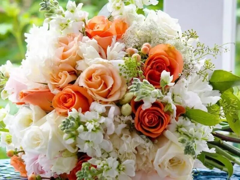 A colorful bridal bouquet with orange, pink, and white roses, along with other beautiful flowers.