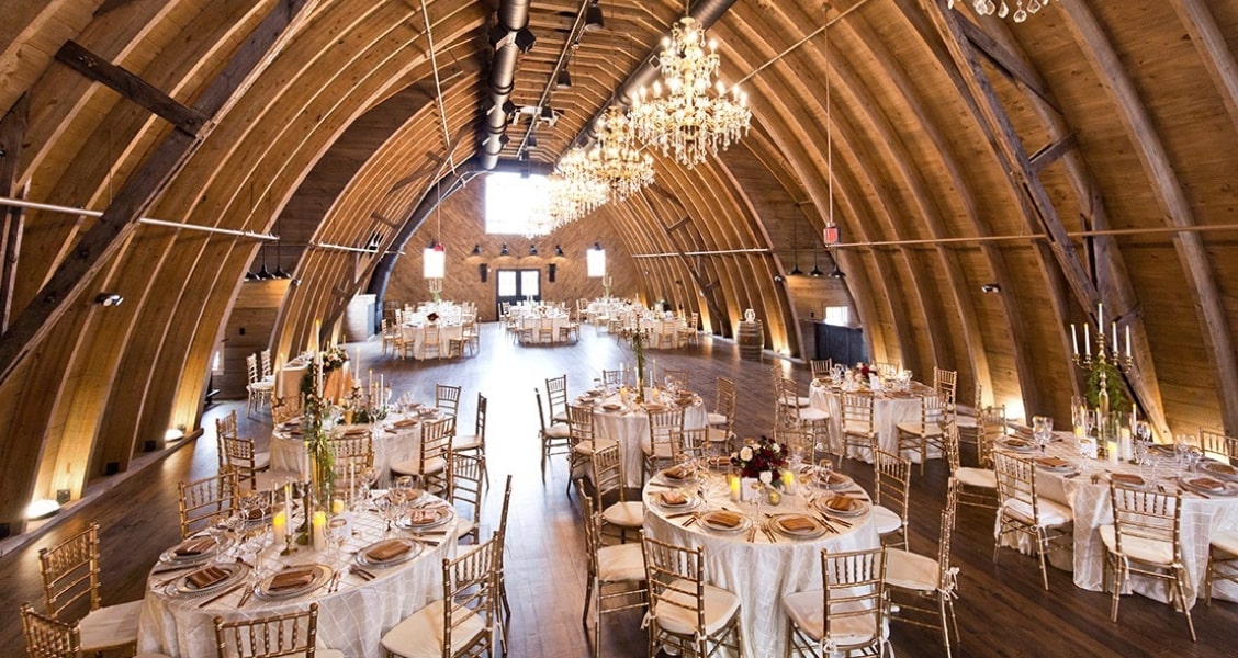 An interior shot of the massive Sweeney Barn, a wedding venue in Virginia with chandeliers hanging from the barn's ceiling.