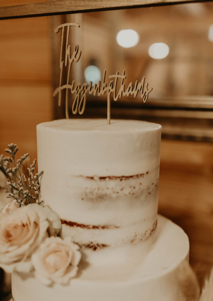 Elegant wedding cake with 'The Higginbothams' topper surrounded by white roses.