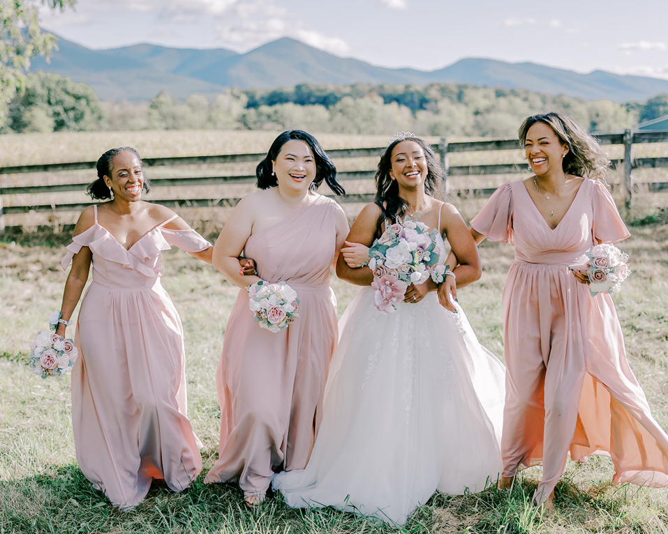 Joyful bridesmaids in pink dresses laughing in a scenic outdoor setting.