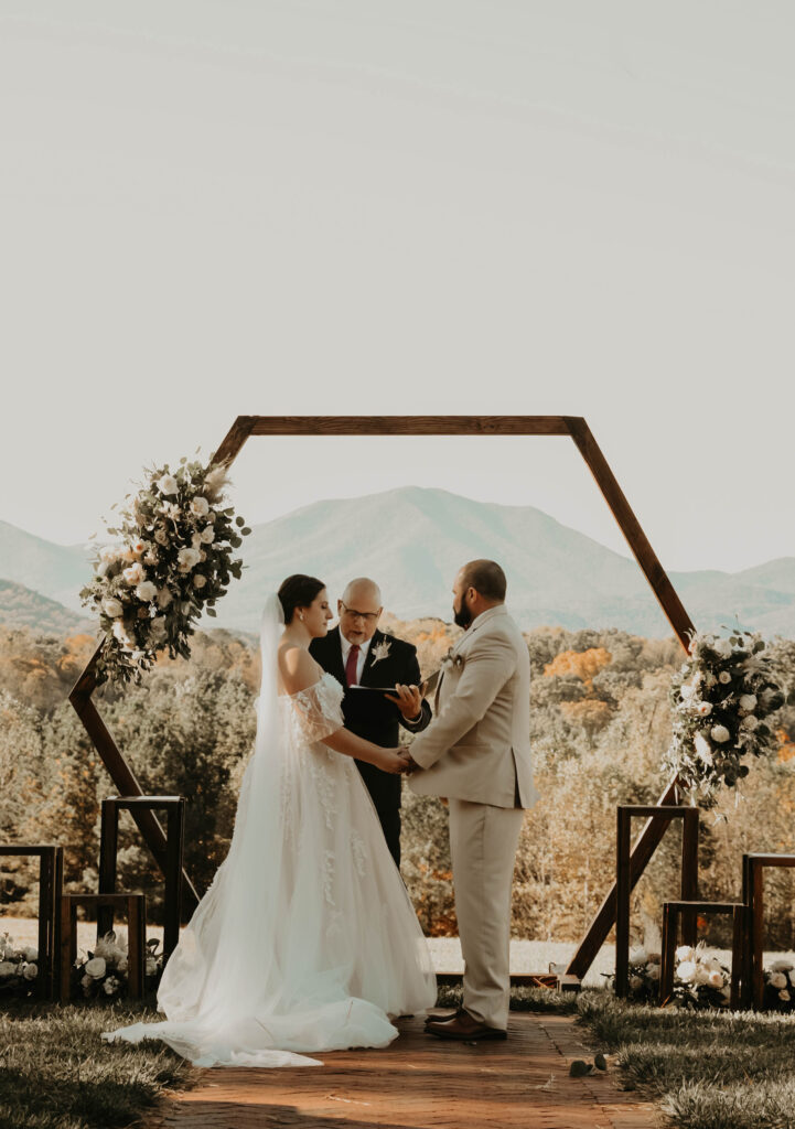 Rustic outdoor wedding ceremony with a couple exchanging vows under a wooden arch.