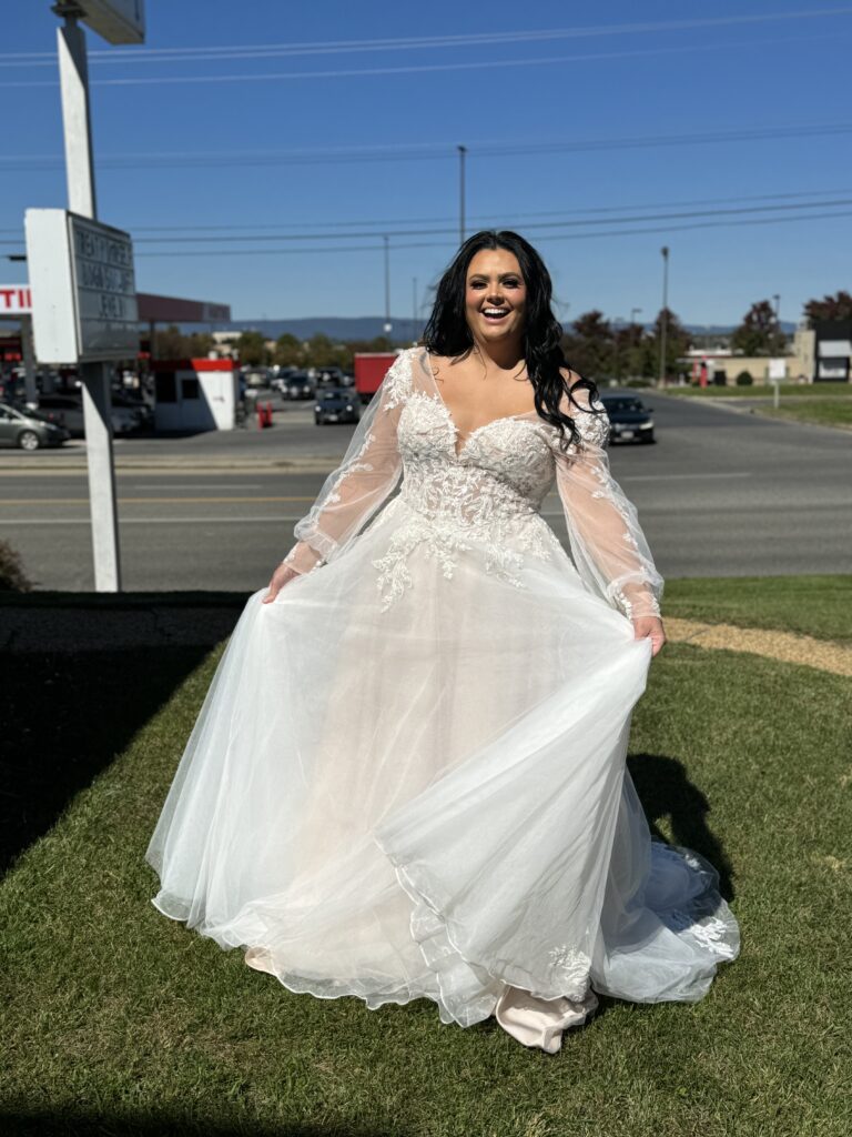 Bride in flowing white gown stands joyously outside, suburban setting in background.