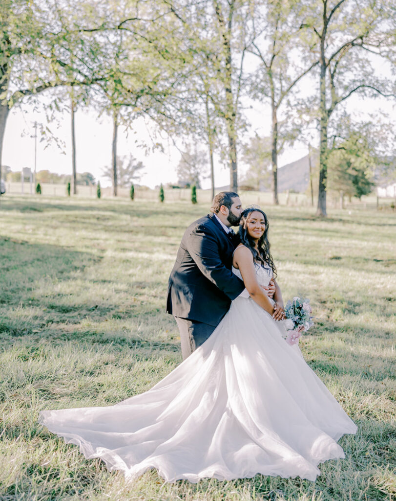 Couple embracing outdoors in a lush field, bride in a flowing gown.