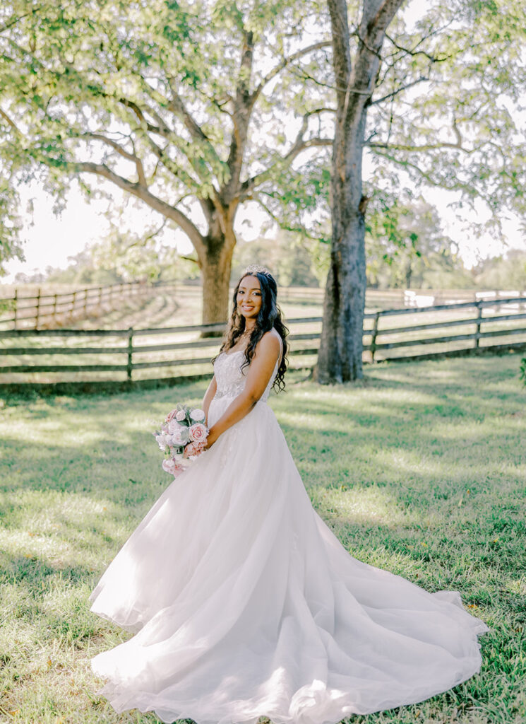 Bride in a flowing gown smiling in a sunlit forest.