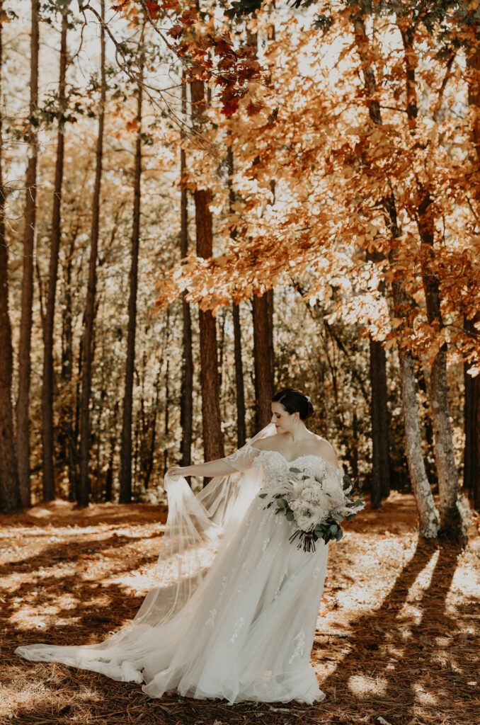 Bride seated amidst autumn leaves, holding a bouquet.