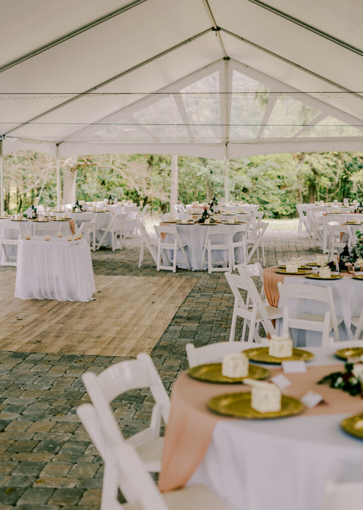 Elegant outdoor tent set up for a wedding with white chairs and tables.