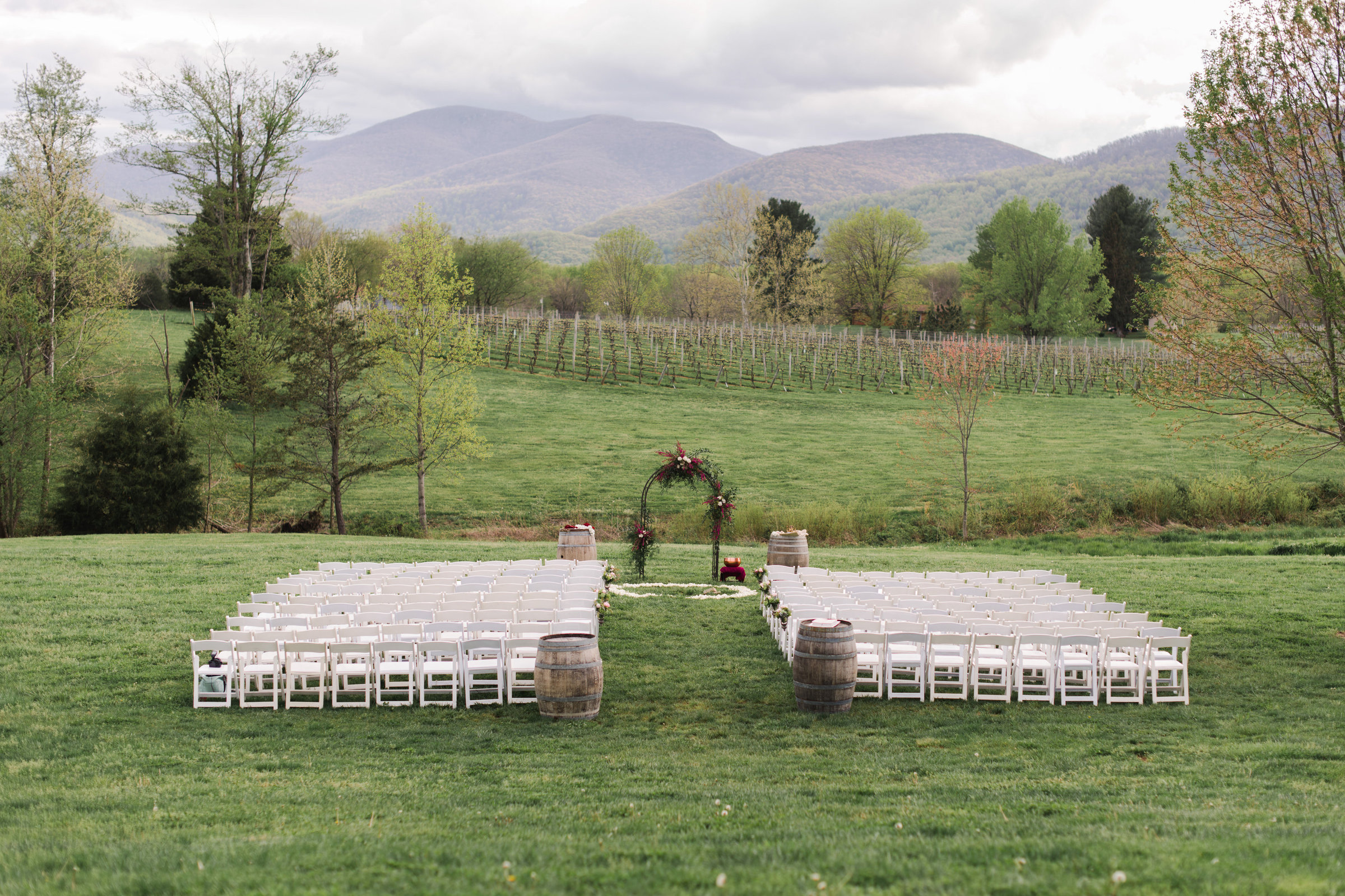 Rustic wedding ceremony with floral arch and white chairs in a Virginia vineyard.