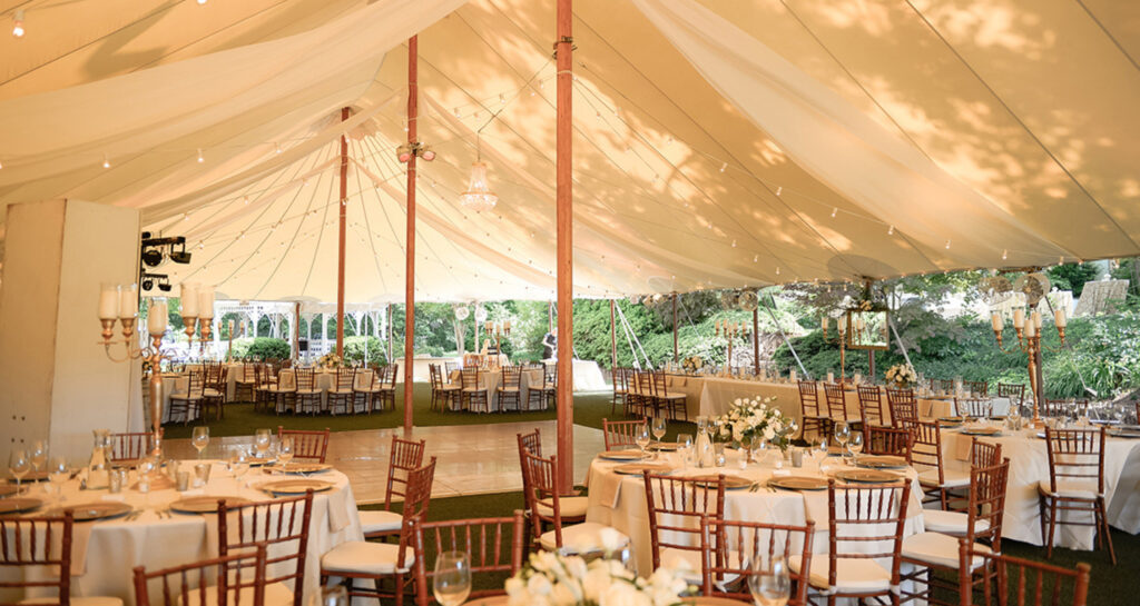 Romantic outdoor wedding reception tables under a large tent with lights.