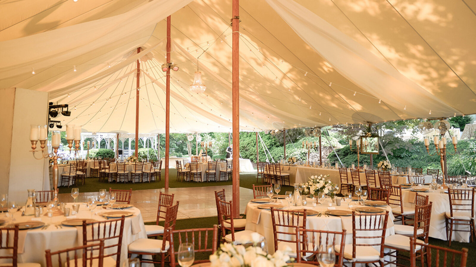 Romantic outdoor wedding reception tables under a large tent with lights.