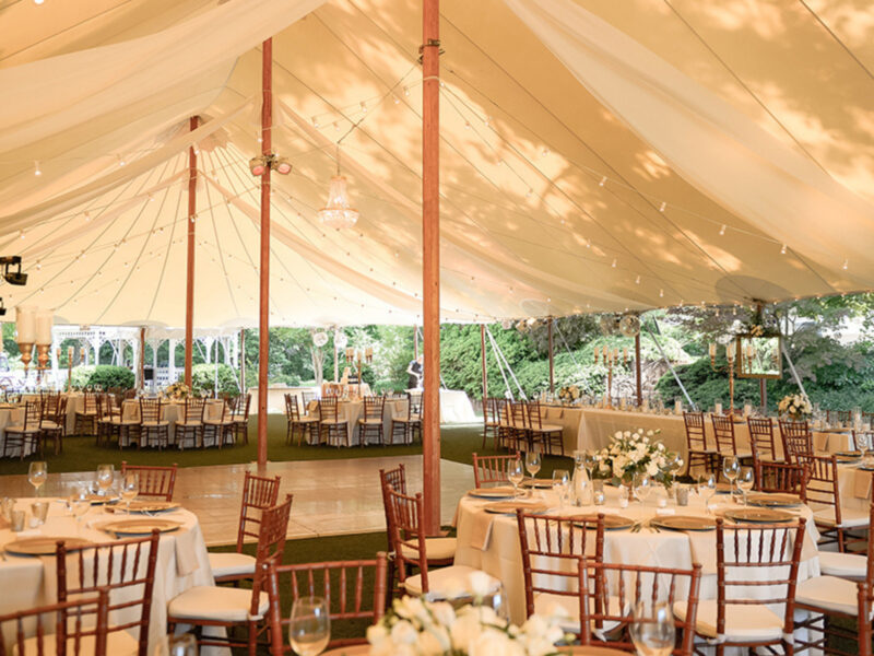 Romantic outdoor wedding reception tables under a large tent with lights.