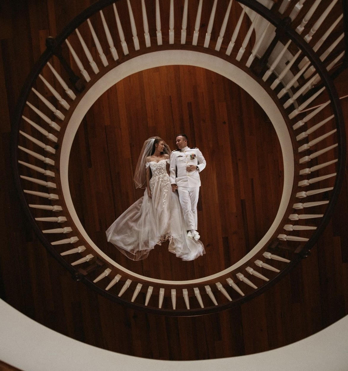 Bride and groom holding hands laying on the wood floor looking at each other lovingly.