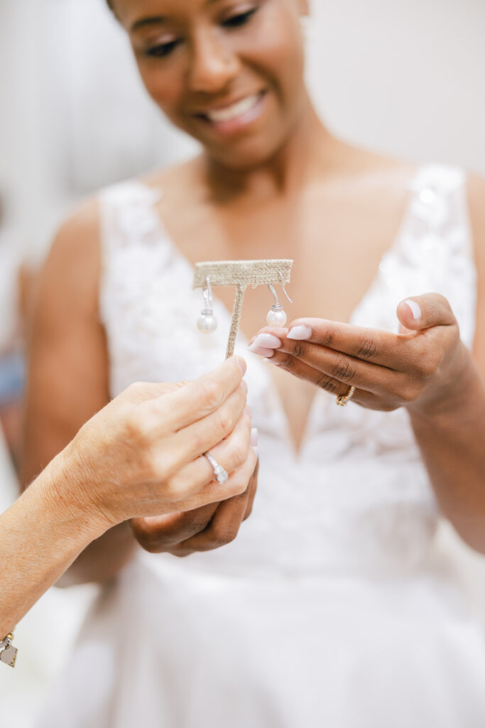 Close-up of a bride admiring a pair of elegant pearl earrings, showcasing her radiant smile and beautiful wedding dress details.