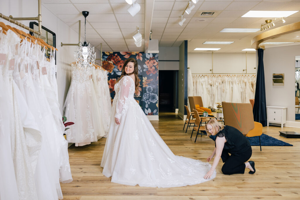 A bridal stylist flattening bride's dress train in a bridal boutique.
