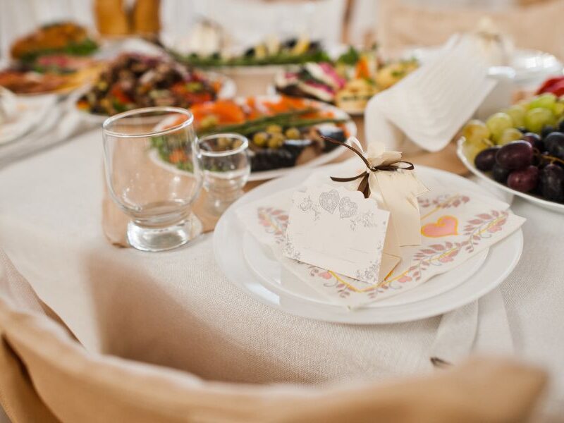 Elegant wedding table setting with a variety of colorful dishes, fresh fruits, and a personalized favor box on a white plate with a floral napkin.