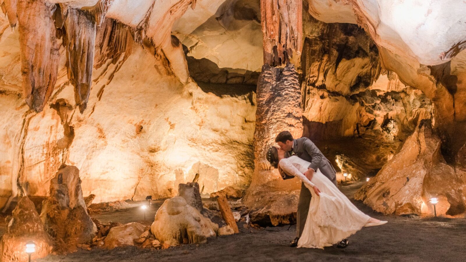 A couple sharing a romantic kiss in a stunning cave venue surrounded by dramatic rock formations and soft lighting.