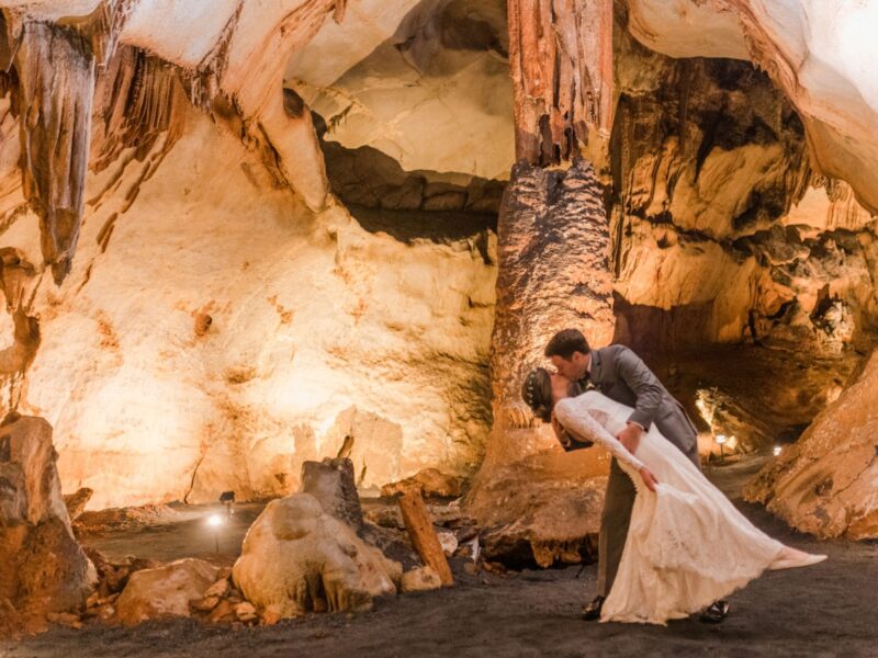 A couple sharing a romantic kiss in a stunning cave venue surrounded by dramatic rock formations and soft lighting.